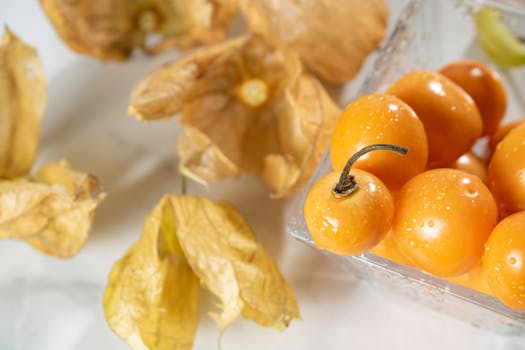 Vibrant close-up of golden cape gooseberries with water droplets in a glass container, surrounded by husks.